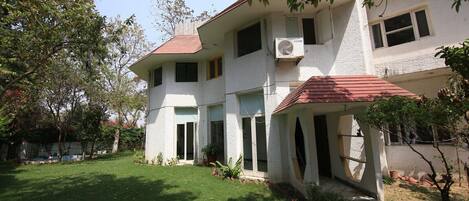A two-story house with a red-tiled roof, a small garden, and an air conditioning unit mounted on the exterior wall.