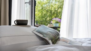Un lit avec un magazine, une tasse et une fenêtre donnant sur un paysage verdoyant.