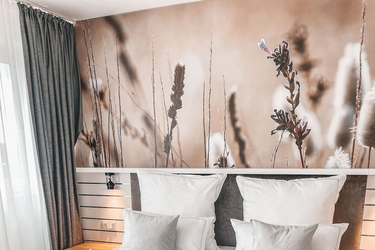 A neatly made bed with white linens and towels, a headboard with a floral mural, and a bedside table with a lamp.