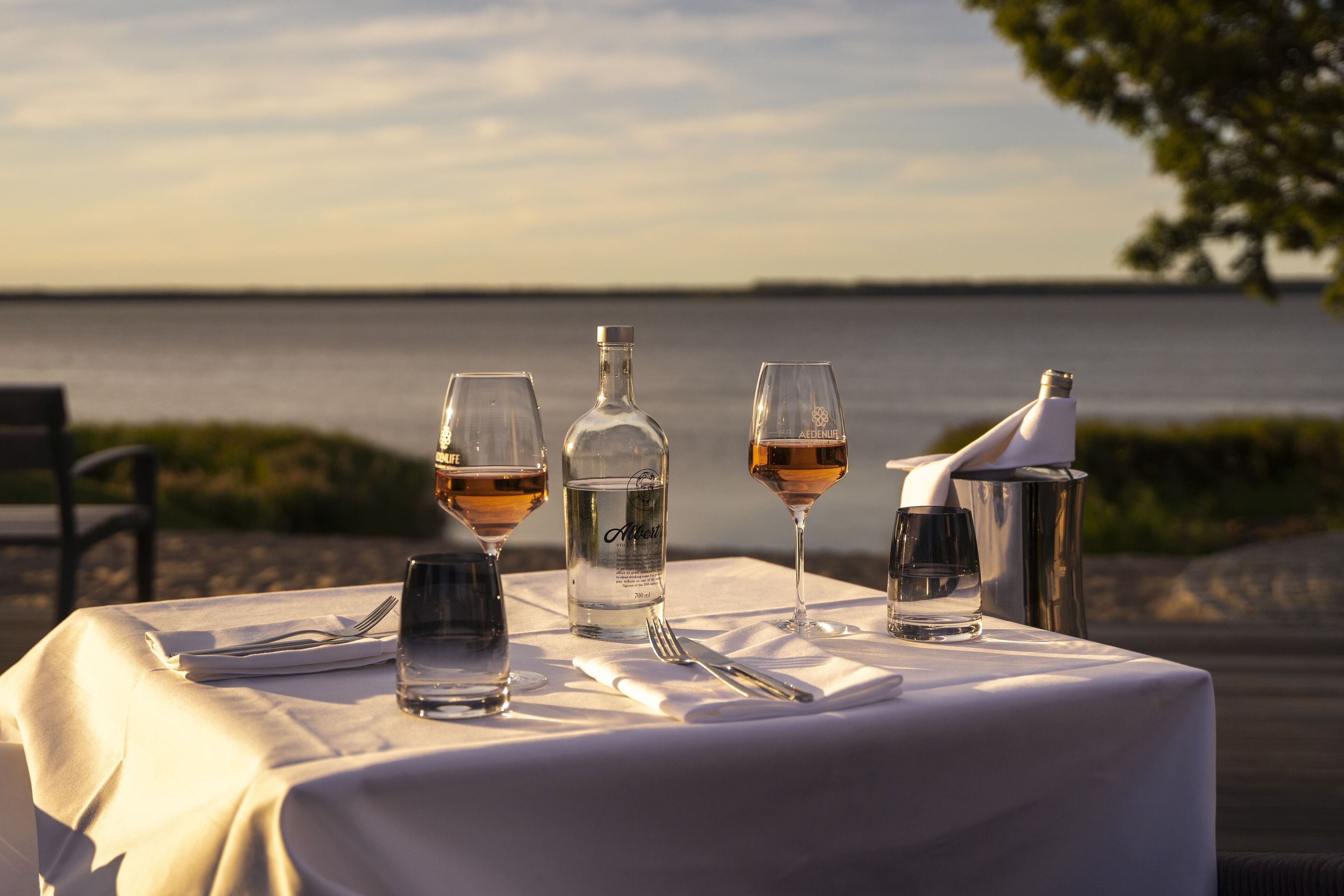 A table set with wine glasses, a bottle, and a pitcher, overlooking a body of water.