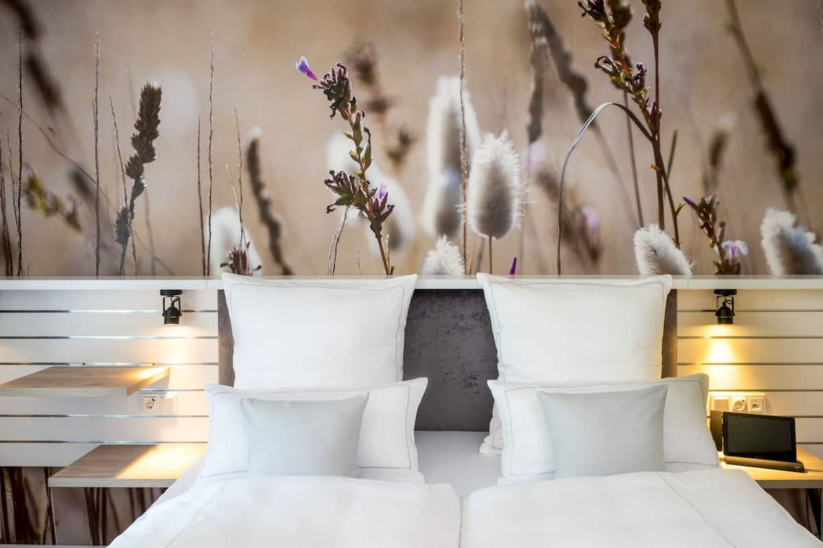 A modern hotel room with a bed, bedside tables, and a wall-mounted shelf.