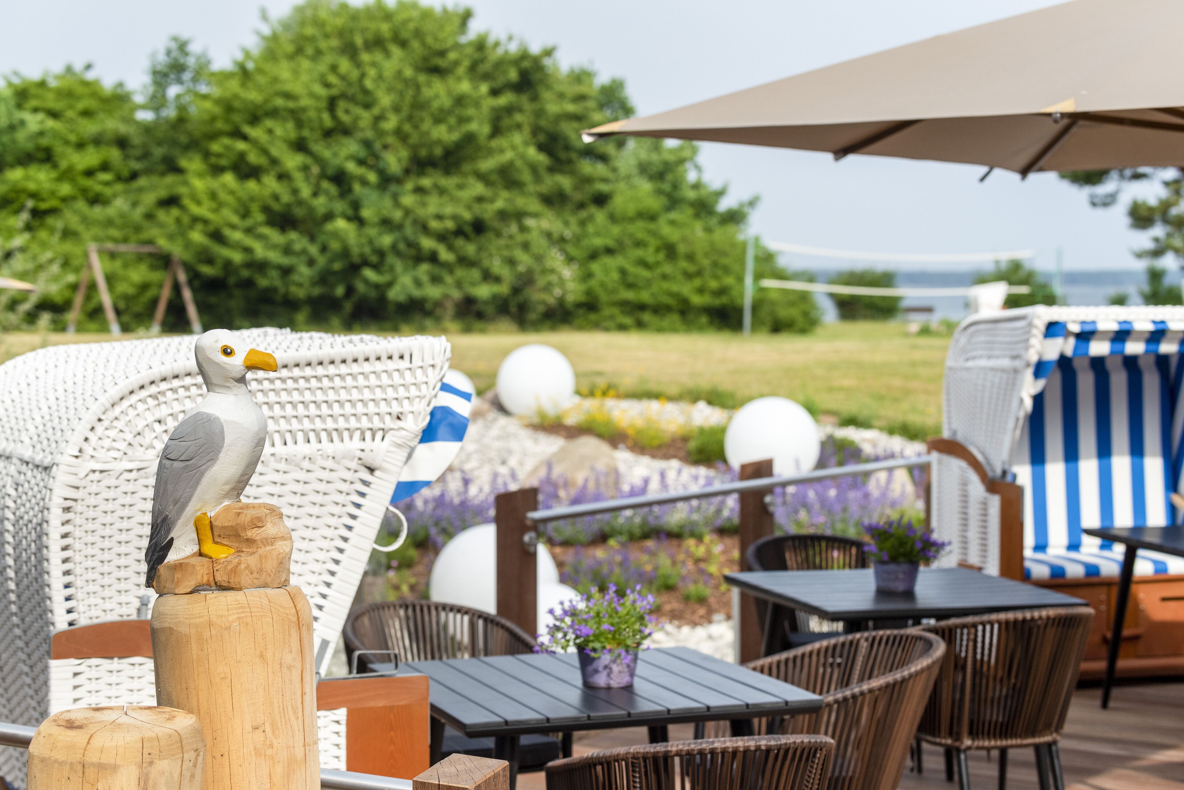 An outdoor seating area with wicker furniture, a wooden post with a bird sculpture, and a view of the sea.