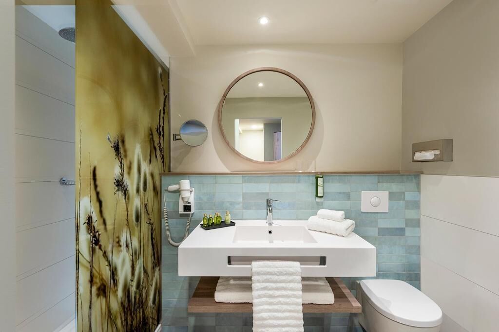 A modern bathroom with a white sink, a round mirror, and a toilet.