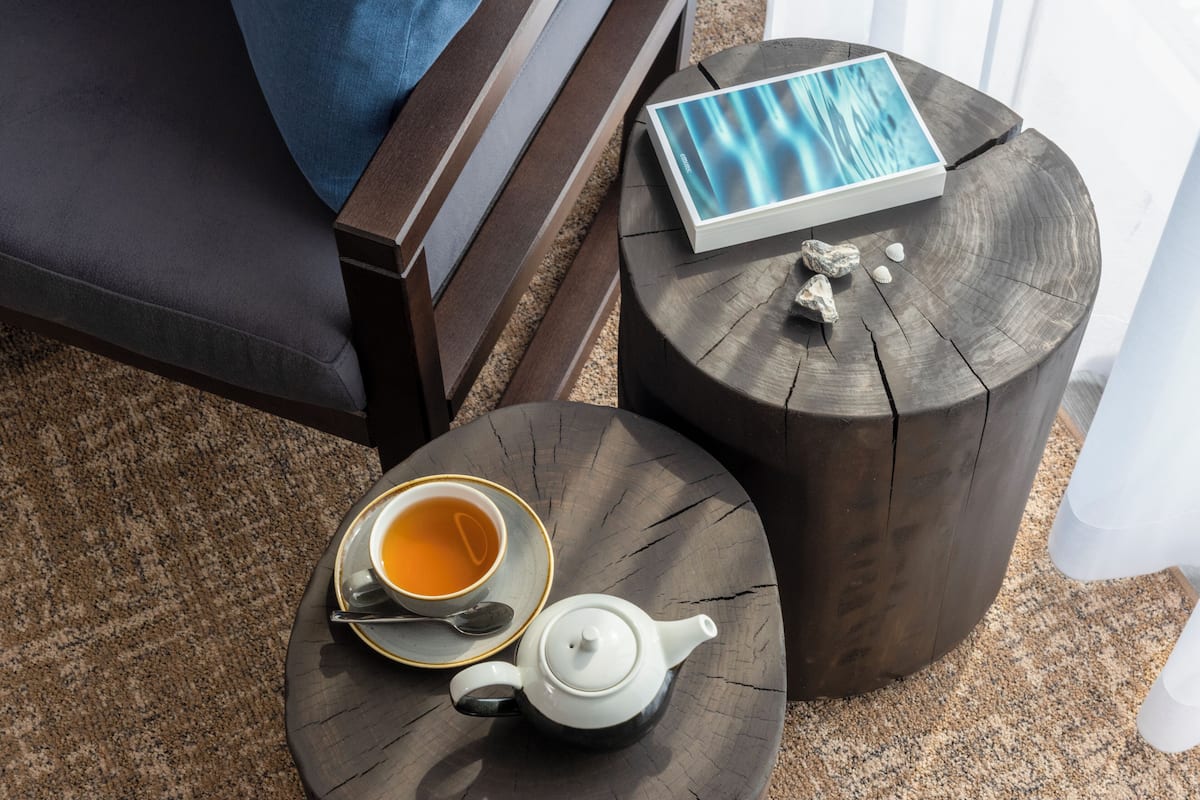 A cozy seating area with a wooden chair, a round wooden table with a teapot and cup, and a book.