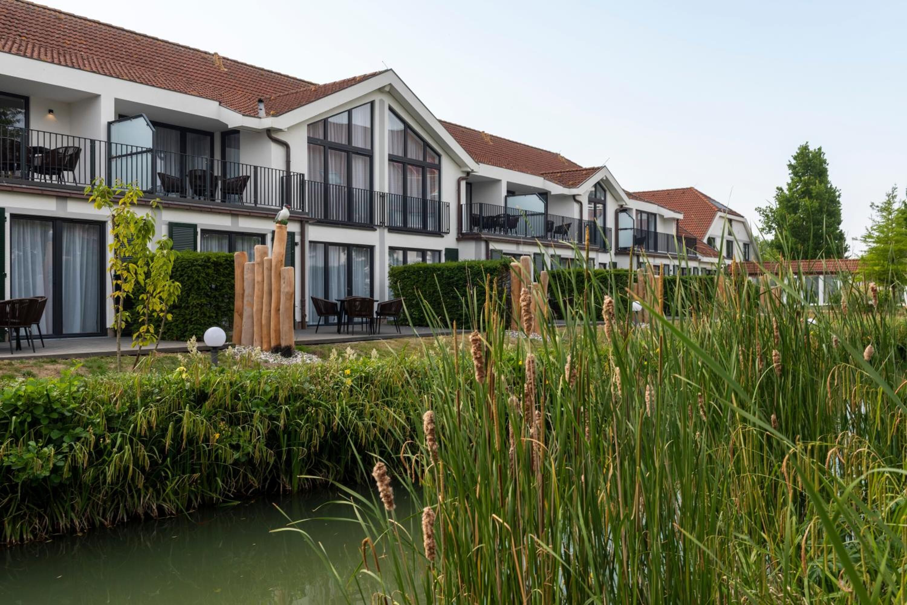A row of modern, two-story buildings with balconies, a small water feature, and lush greenery.
