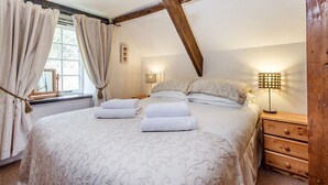 Une chambre à coucher avec un grand lit, deux tables de chevet, une tête de lit en bois et une fenêtre avec des rideaux.