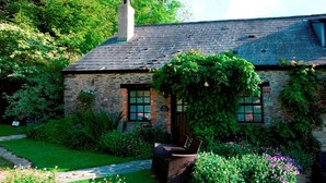 Une charmante maison en pierre aux murs recouverts de lierre, dotée d’une cheminée et d’un jardin agrémenté d’un sentier et de mobilier d’extérieur.