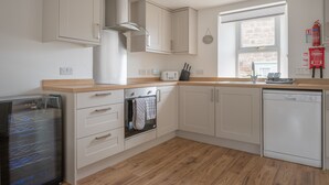 A modern kitchen with white cabinetry, a built-in oven, a dishwasher, and a window providing natural light. - Beautiful Detached House, just meters from the sea (Gourdon)