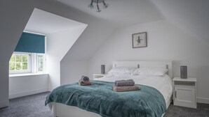A bedroom with a sloped ceiling, a bed with white bedding, a teal blanket, two bedside tables with lamps, and a window with a blue blind. - Beautiful Detached House, just meters from the sea (Gourdon)
