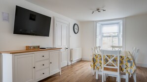 A compact kitchen with a TV, white cabinets, a wooden countertop, and a dining area with a yellow tablecloth. - Beautiful Detached House, just meters from the sea (Gourdon)