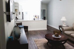 Ein modernes Wohnzimmer mit dunklem Holzboden, einem runden Couchtisch, einem beigen Sofa und einem kleinen Beistelltisch mit Lampe.
