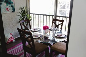 A dining table set for four with chairs, a glass top, and a pink flower centerpiece.