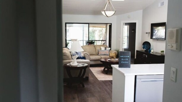 A modern living room with a sofa, coffee table, and a dining area with a refrigerator. - Immaculate Fort Myers Condo, ideal location-quiet (Fort Myers)