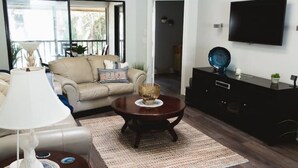 A living room with a sofa, a coffee table, a lamp, a TV, and a black cabinet. - Immaculate Fort Myers Condo, ideal location-quiet (Fort Myers)