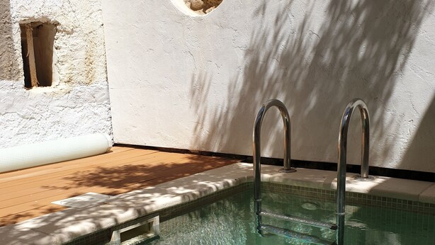 A swimming pool with clear water, a stone wall, and a small circular window. - La Félicita - Charming gîte near Narbonne (Moussan)