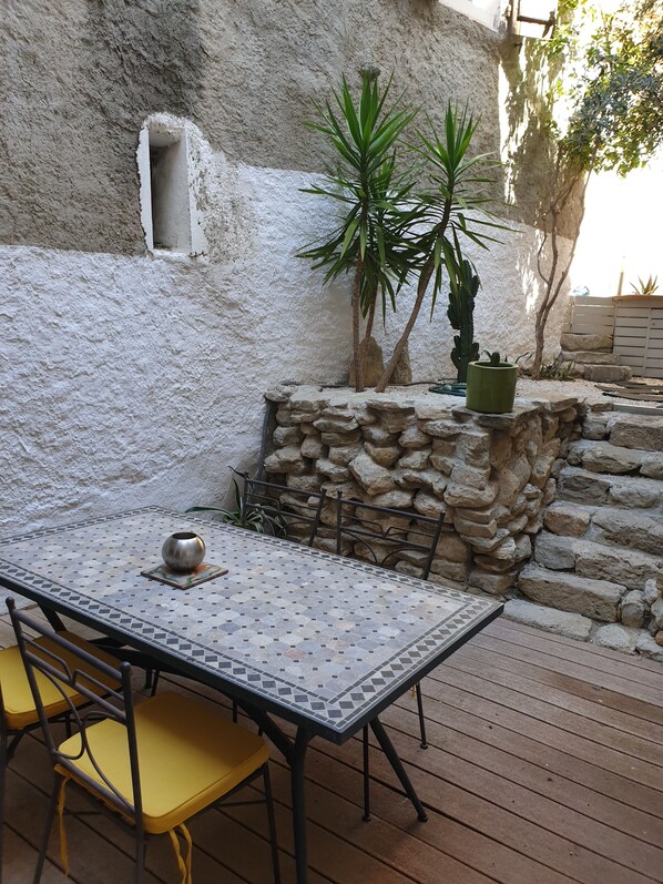 Eine Terrasse mit Tisch, Stühlen, einer Steinmauer und Topfpflanzen.
