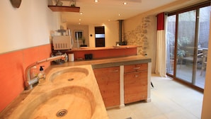 A kitchen with a double sink, wooden cabinets, a built-in stove, and a sliding glass door to a patio. - La Félicita - Charming gîte near Narbonne (Moussan)