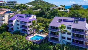 Ein mehrstöckiges Hotel mit Pool auf dem Dach, umgeben von üppiger Vegetation und Blick aufs Meer.