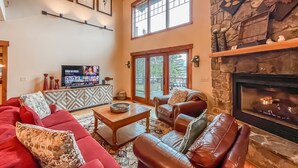 A cozy living room with a fireplace, a television, and a large window. - Walk to Wisp! Flat Lakefront + Fire Pit and Huge Dock! (McHenry)