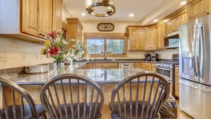 A modern kitchen with wooden cabinets, stainless steel appliances, and a central island with chairs. - Walk to Wisp! Flat Lakefront + Fire Pit and Huge Dock! (McHenry)