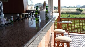 A bar area with bottles, glasses, and stools. - Danaos Beach Apartments (Rethymno)