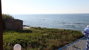 A coastal view with a person swimming in the sea, a wooden structure, and a railing with a striped cover. - Danaos Beach Apartments (Rethymno)