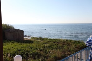 A coastal view with a person swimming in the sea, a wooden structure, and a railing with a striped cover.