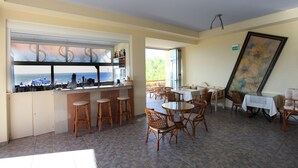A restaurant with a bar area, wicker chairs, and a view of the sea. - Danaos Beach Apartments (Rethymno)