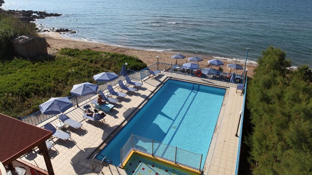 A swimming pool with lounge chairs and umbrellas, a beach, and the ocean. - Danaos Beach Apartments (Rethymno)