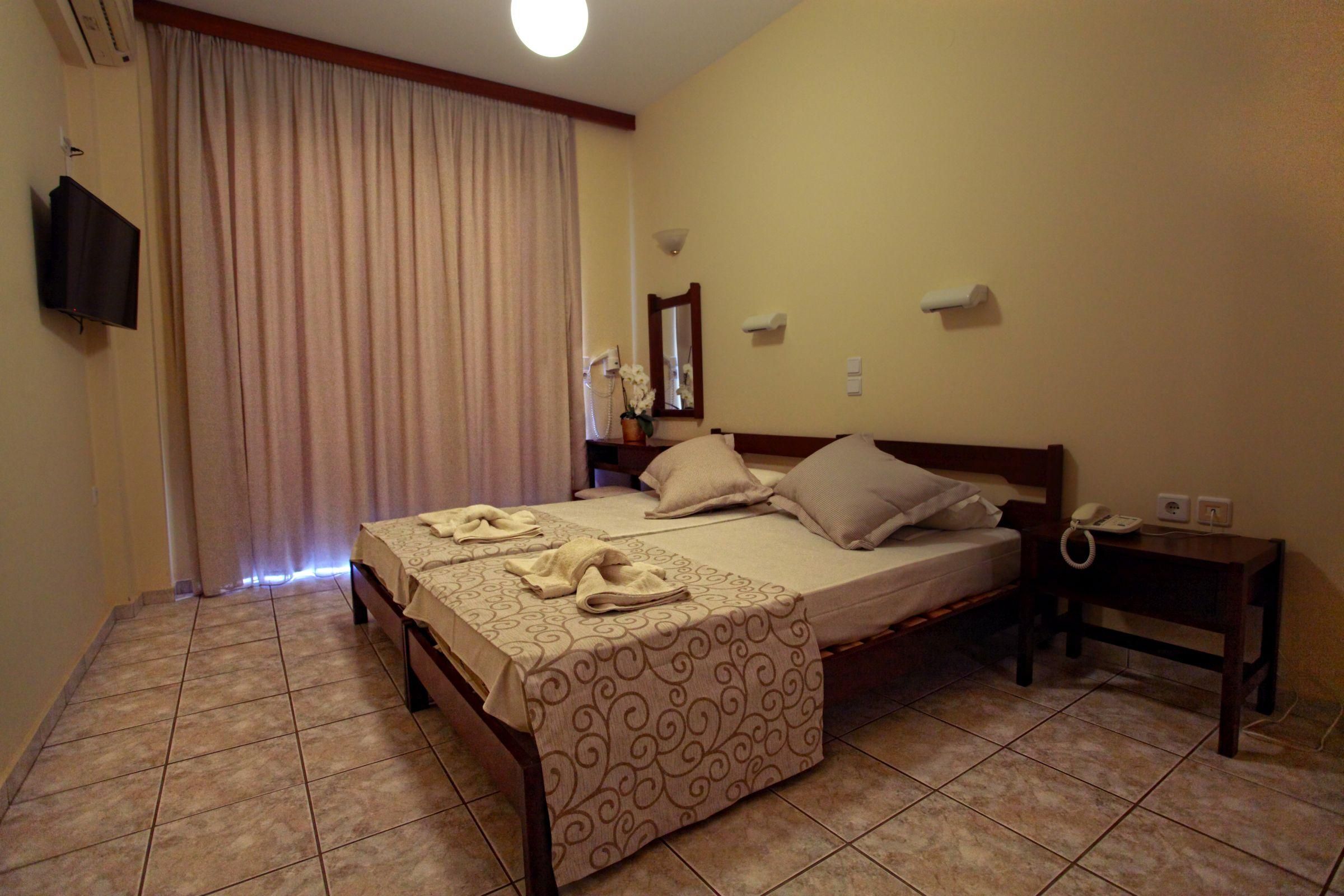 Une chambre d’hôtel avec un lit, une table de chevet, une télévision, un miroir et une fenêtre avec des rideaux.