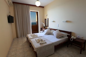 A hotel room with two beds, a bathroom, a TV, and a view of the sea. - Danaos Beach Apartments (Rethymno)