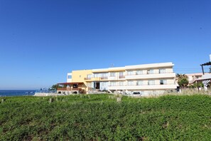 A multi-story hotel with balconies, a pool area, and a view of the sea.