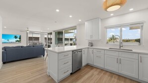 A modern kitchen with white cabinetry, a built-in dishwasher, and a large window.