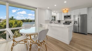 A modern kitchen with white cabinetry, a stainless steel refrigerator, and a dining area with wicker chairs.