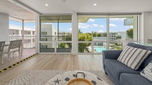 A spacious living room with a balcony, large windows, and a view of a swimming pool.
