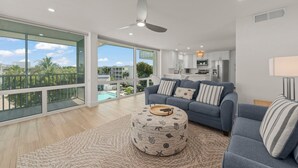 A modern living room with a large sofa, ottoman, and a view of a swimming pool.