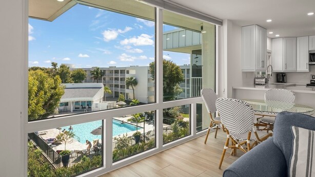A modern apartment with large windows, a balcony with a pool view, and a kitchenette.
