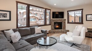 A modern living room with a gray sectional sofa, a white armchair, a glass coffee table, and a stone fireplace. - Mountainback at Mammoth Lakes (Mammoth Lakes)