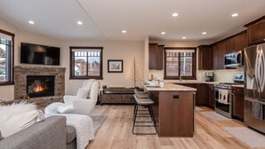 A modern kitchen with a stone fireplace, wooden cabinets, and a central island. - Mountainback at Mammoth Lakes (Mammoth Lakes)