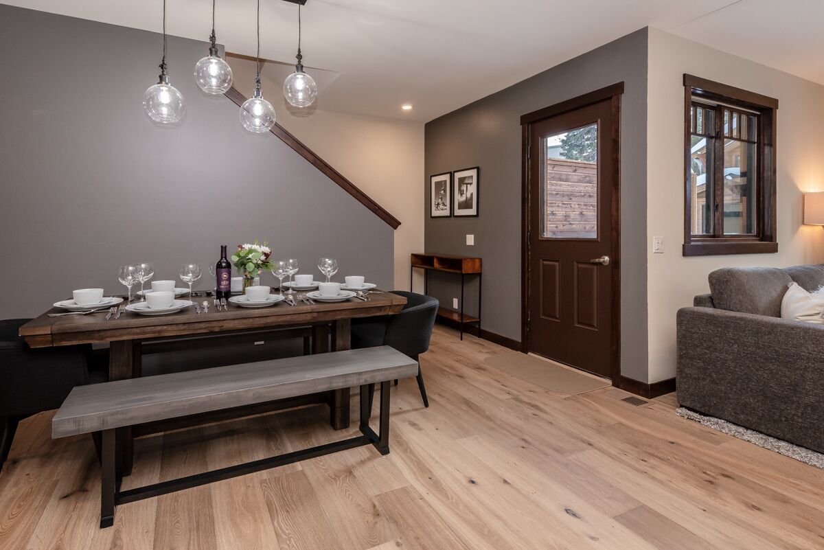 A dining area with a wooden table set for four, a bench, and a dark wooden door with a window.