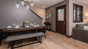 A dining area with a wooden table set for four, a bench, and a dark wooden door with a window.