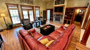 Amplia sala de estar con un sofá grande de cuero rojo, chimenea y piso de madera.