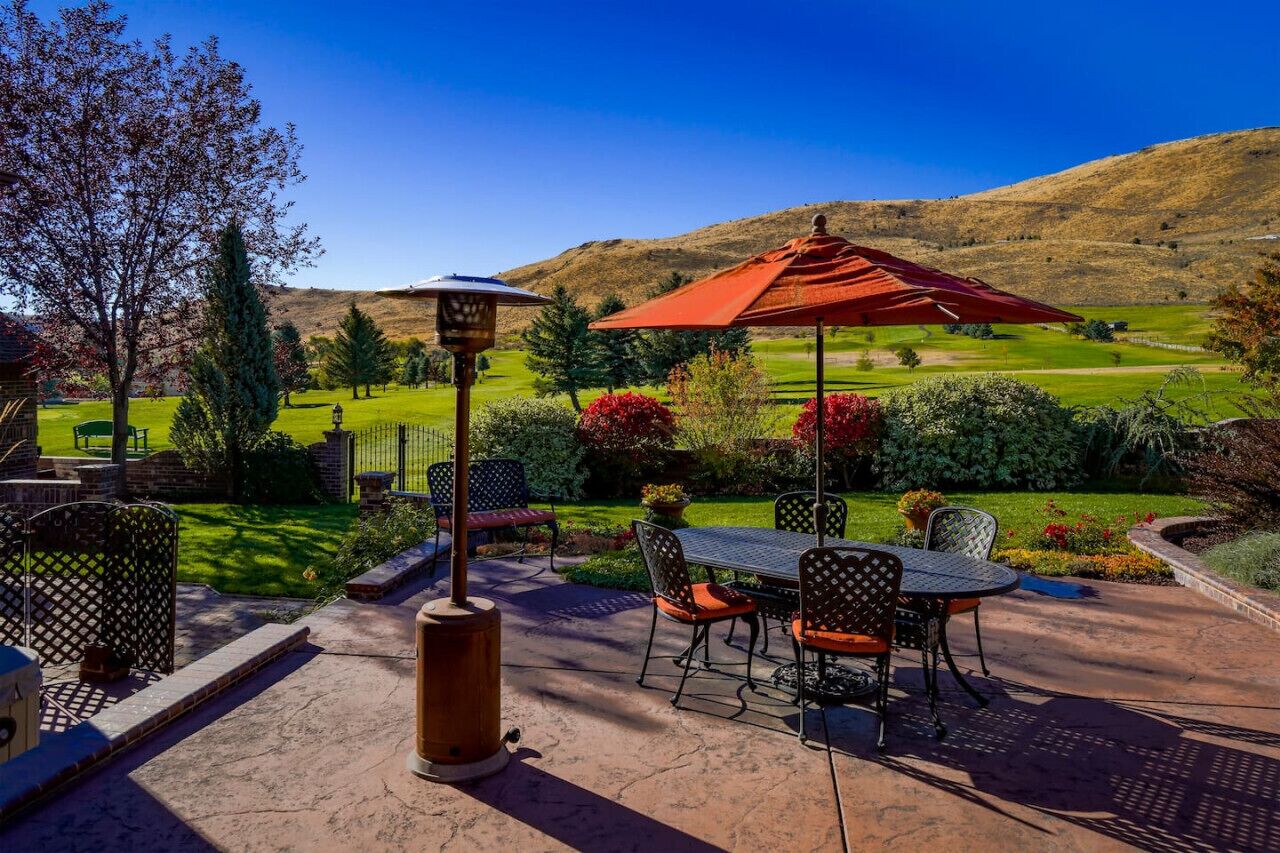 An outdoor patio with a table and chairs, a red umbrella, and a view of a golf course and hills in the background.