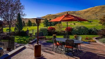 An outdoor patio with a table and chairs, a red umbrella, and a view of a golf course and hills in the background.