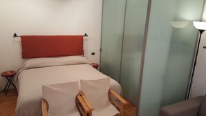 Une chambre à coucher avec un lit, une chaise en bois, une tête de lit rouge, une table de chevet et une lampe sur pied.