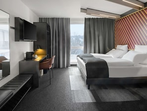 Une chambre d’hôtel moderne équipée d’un lit, d’un bureau avec une chaise, d’une télévision et offrant une vue sur l’extérieur.