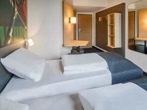 A hotel room with two beds, a small table, a mirror, and a wall-mounted shelf. - B&B Hotel Bad Homburg (Bad Homburg v.d. Hoehe)