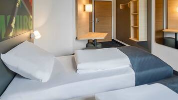 Habitación de hotel con dos camas, una mesita, un espejo y una estantería en la pared.