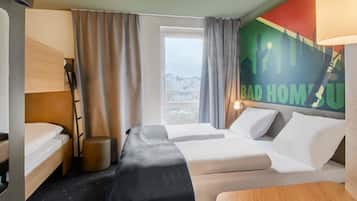 Ein Hotelzimmer mit zwei Betten, einem Schreibtisch, einem Stuhl, einem Fenster mit Vorhängen und einer Wand mit einem Stadtlandschaftsposter.