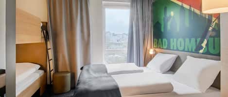 A hotel room with two beds, a desk, a chair, a window with curtains, and a wall with a cityscape poster.
